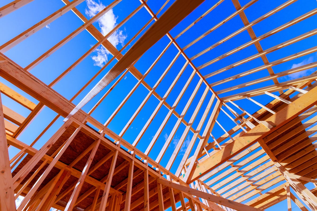 Workers constructing wooden frame beams for a new building under roof trusses