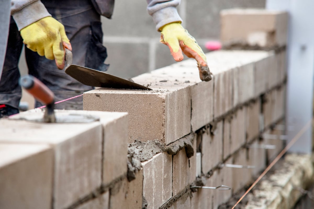 A construction worker placing concrete blocks on a wall with a trowel